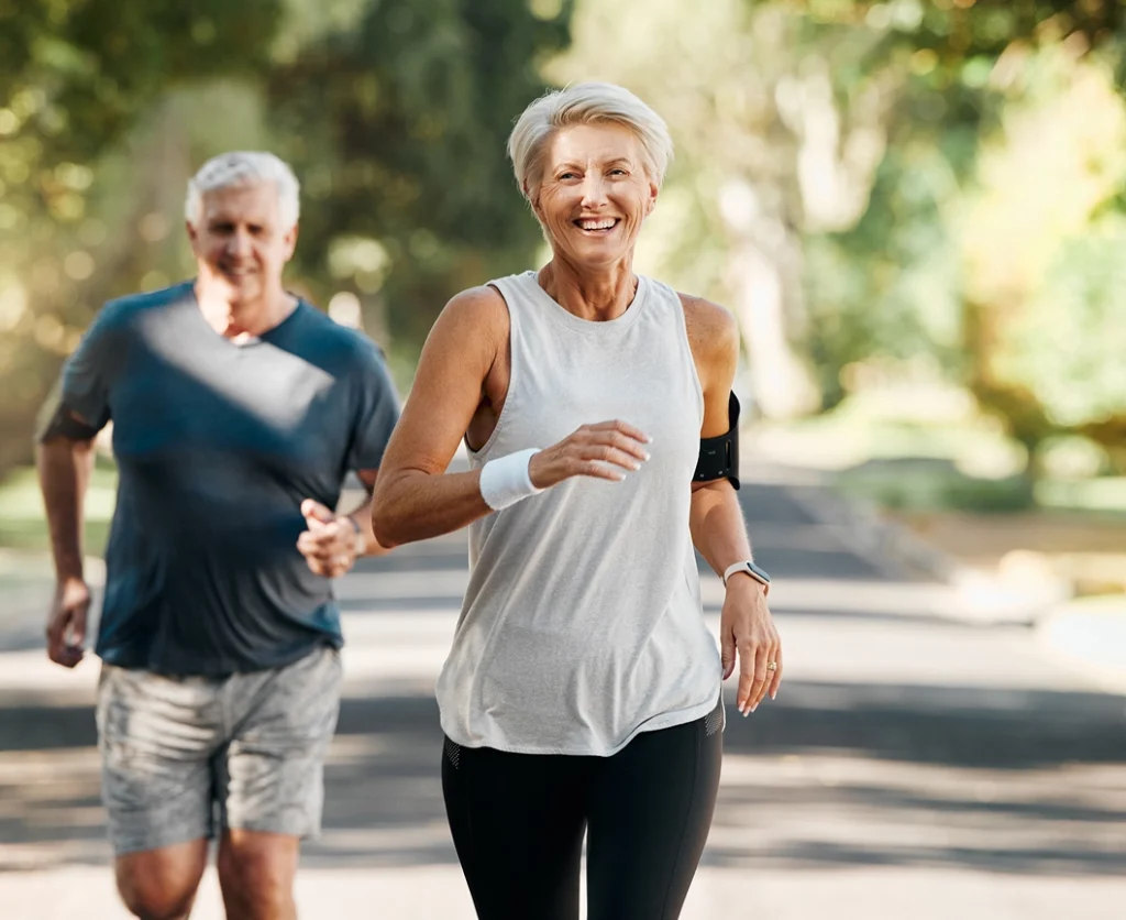 Hombre y mujer mayores corriendo en un parque y sonriendo a cámara, ejemplo de vida activa en la silver economy.