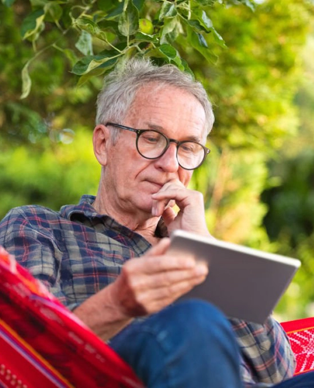 Hombre mayor sentado en una hamaca leyendo en una tablet, ejemplo de autonomía digital en la silver economy.