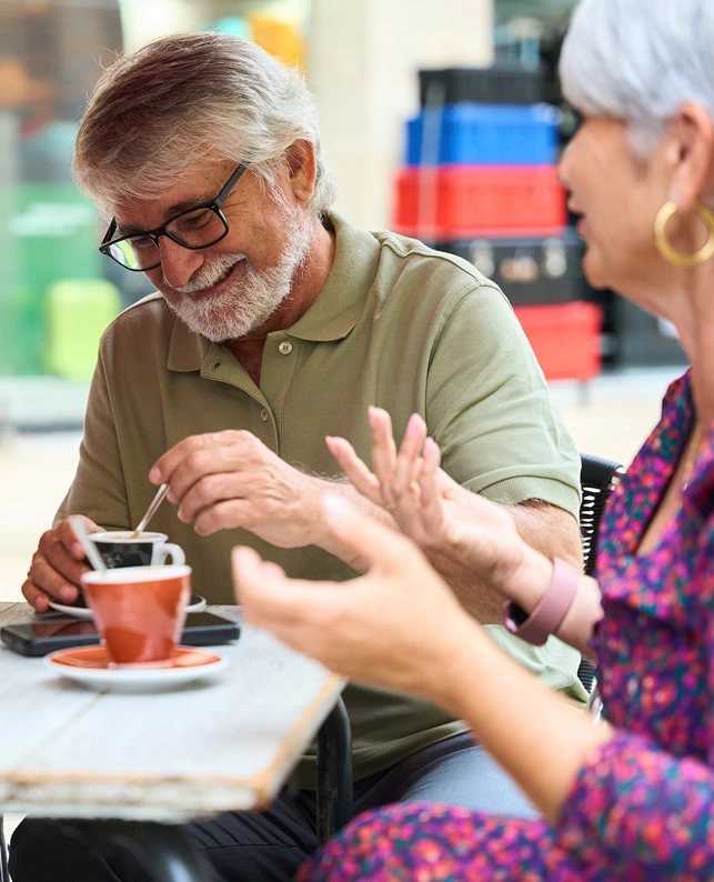Hombre y mujer mayores conversando mientras toman café en una terraza, ejemplo de interacción cercana en la silver economy.