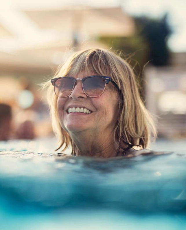 Mujer adulta con gafas de sol sonriendo mientras se refresca en el agua, ejemplo de bienestar y envejecimiento activo en la silver economy.